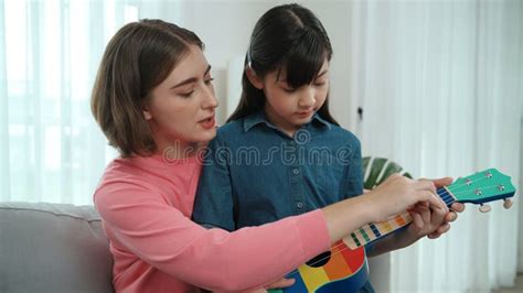 Happy Girl Playing Ukulele While Caucasian Mom Teaching And Explain