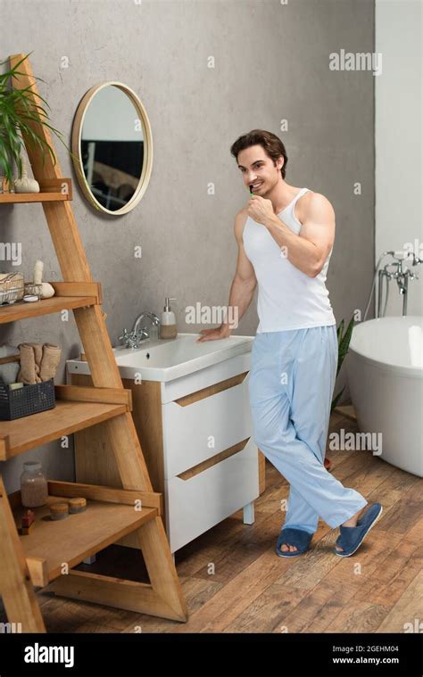 Man In White Tank Top And Blue Pajama Pants Standing Near Sink In