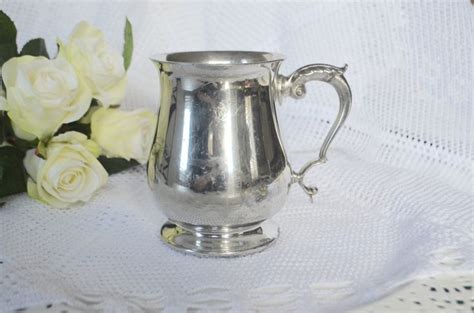 A Silver Cup Sitting On Top Of A Table Next To White Flowers And A Lace