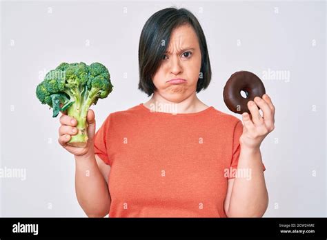 Brunette Woman With Down Syndrome Holding Broccoli And Chocolate Donut