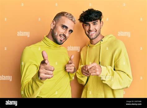 Homosexual Gay Couple Standing Together Wearing Yellow Clothes Pointing Fingers To Camera With