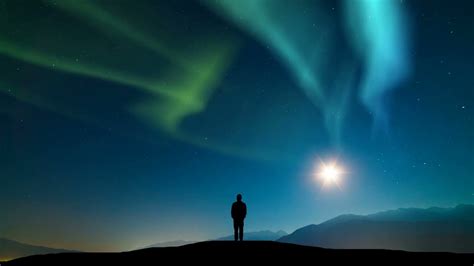 The Man Standing On A Mountain Against The Sky With A Northern Light