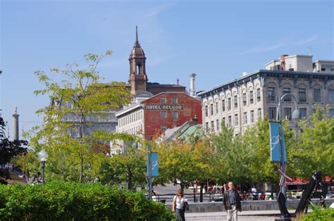 some people are walking around in the city with tall buildings and green trees on both sides