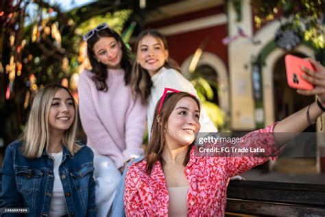 Young Women Taking Selfies Or Filming Using Mobile Phone Outdoors High