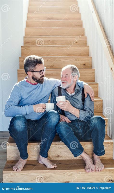 An Adult Hipster Son And Senior Father Sitting On Stairs Indoors At