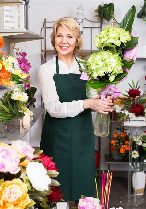 Female Florist Wearing An Apron And Happily Standing Among Flowers