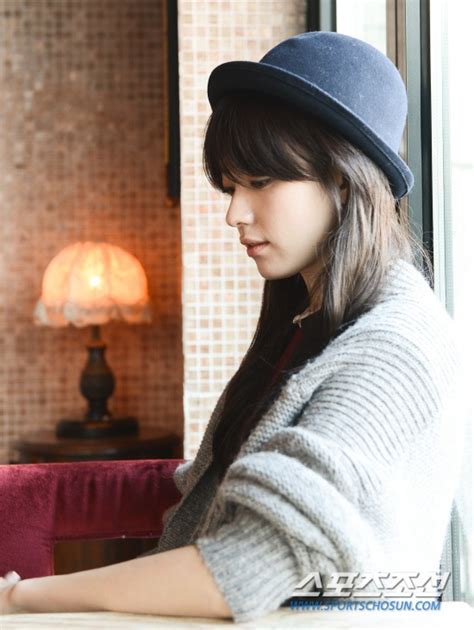 A Woman Sitting At A Table In Front Of A Window With A Hat On Her Head