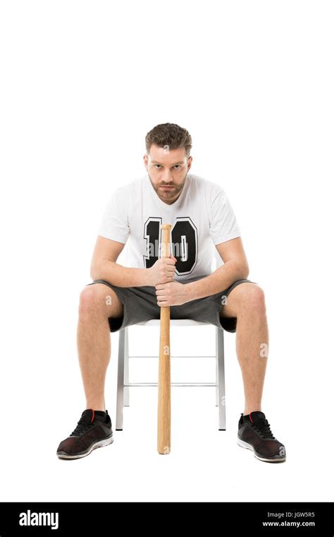 Serious Man Holding Baseball Bat While Sitting On Chair Isolated On