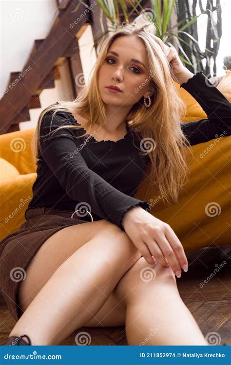 Blonde With Long Beautiful Legs At Home On The Floor Near The Sofa