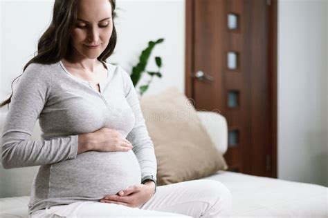 Beautiful Pregnant Woman Sitting On Couch With Hands On Pregnant Belly