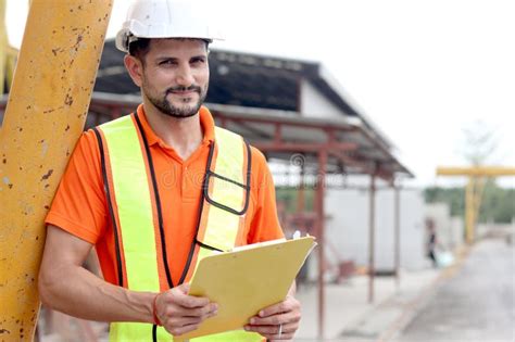 Portrait Of Happy Worker Engineer With Safety Vest And Helmet Holding