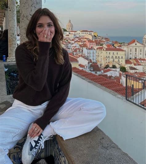 A Woman Is Sitting On A Ledge With Her Hand In Her Mouth And Looking At