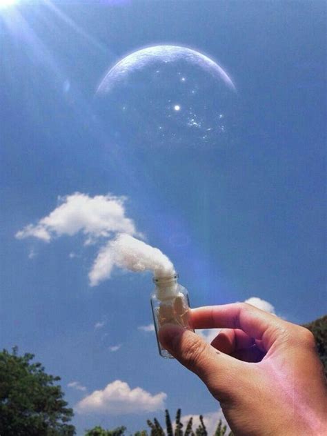 a hand holding an object in front of a blue sky with clouds and the sun