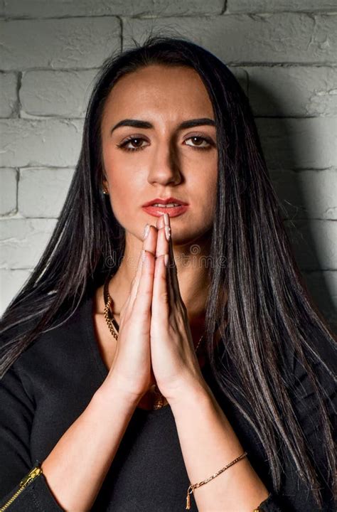Girl Brunette In Black Dress Near The White Brick Wall Folded Her Hands