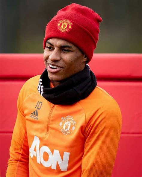 A Man In An Orange Shirt And Red Hat Smiles While Wearing A Scarf