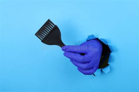 Stylist S Hand Hold Hair Dye Brush Through A Ragged Hole In Blue Paper