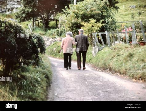 Elderly Couple Walking Arm In Arm Down Country Road Yorkshire England