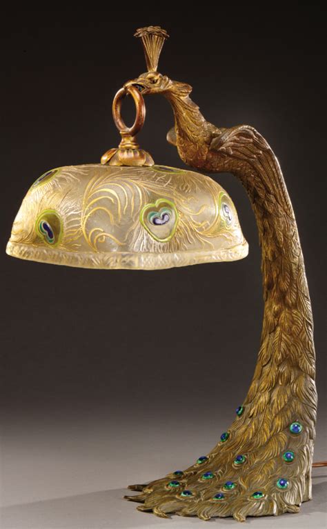 A Large Bronze Lamp Representing A Peacock Holding A Glass Shade Decorated With Peacock Feathers