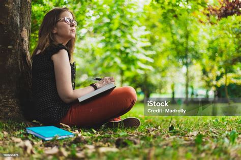 Woman Taking Notes While Making Research From A Book Outdoors Stock