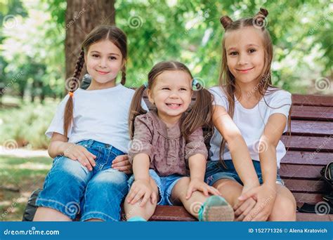 Three Cute Little Girls Smiling And Sitting On The Wooden Bench In