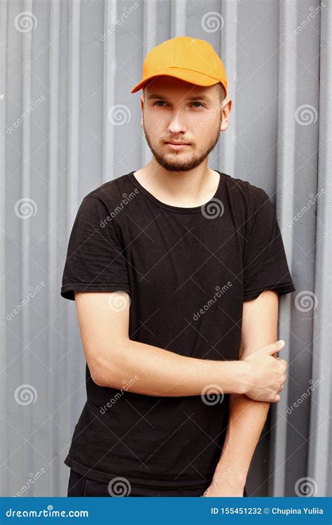 Handsome Guy In A Yellow Cap And Black T Shirt Near A Metal Wall Stock