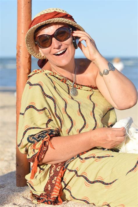 Happy Mature Woman Sitting On Beach And Knitting On Summer Outdoors