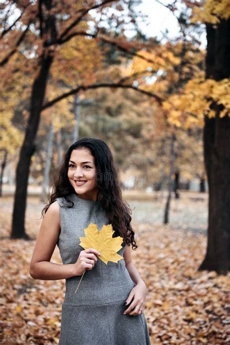 Pretty Woman Posing With Maple`s Leaf In Autumn Park Near Big Tree