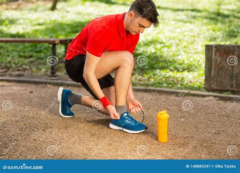 Handsome Young Runner Tying Shoelaces On The Track In The Spring Park