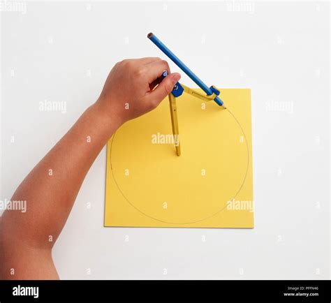 Using Pair Of Compasses And Pencil To Draw Circle On Piece Of Yellow