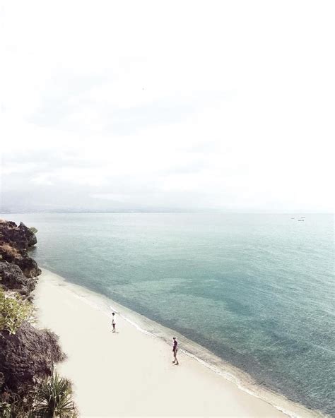 Two People Are Walking On The Beach Next To The Water And Trees In The