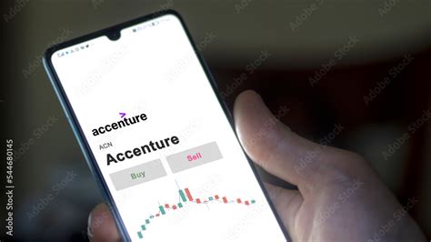 An investor's analyzing the Accenture ACN stock on screen. A phone shows the prices to invest ...