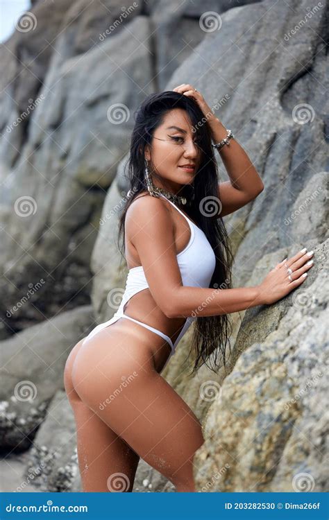 Bella Hispana En Un Bikini Blanco Posando En Una Playa Con Rocas Foto De Archivo Imagen De