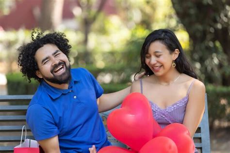 Joven pareja latina mexicana riendo y hablando en el día de san valentín con globos rojos en