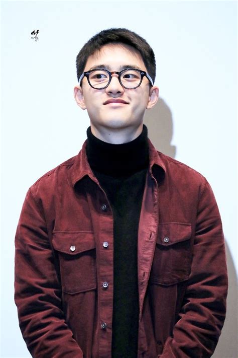 A Man With Glasses Standing In Front Of A White Wall Wearing A Red