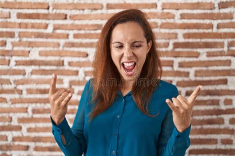 Brunette Woman Standing Over Bricks Wall Shouting With Crazy Expression Doing Rock Symbol With