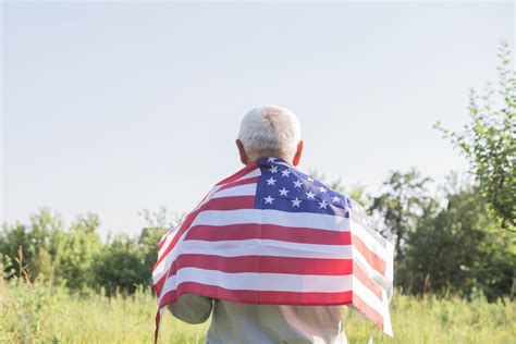 Older Man With American Flag Draped Over Back Standing Outside Facing