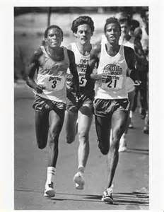 Black And White Photograph Of Three Men Running In A Race With Numbers