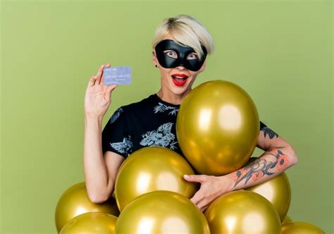 Impressionné Jeune Fille Blonde Portant Un Masque De Mascarade Debout Derrière Des Ballons