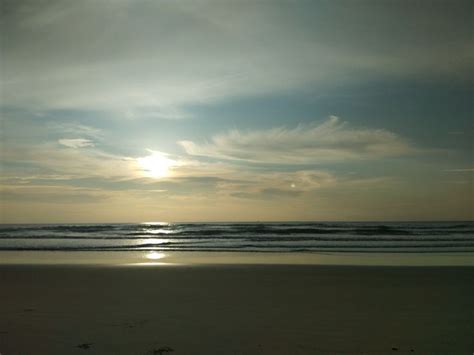 The Sun Is Setting Over The Ocean With Clouds In The Sky And Footprints