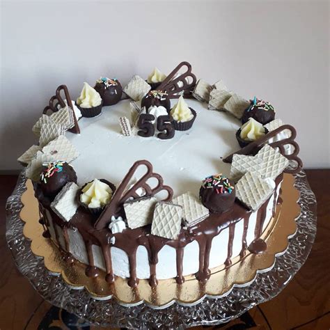 A Cake With White Frosting And Chocolate Toppings On A Glass Platter