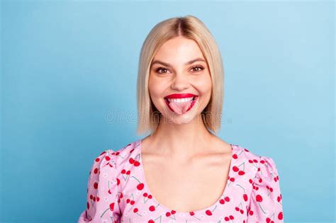 Blonde Woman In A Cherry Print Blouse Smiling And Showing Her Tongue Against A Light Blue
