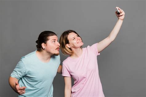 Mujer Joven Sonriente Que Toma El Selfie Con Su Novio Contra Fondo Gris