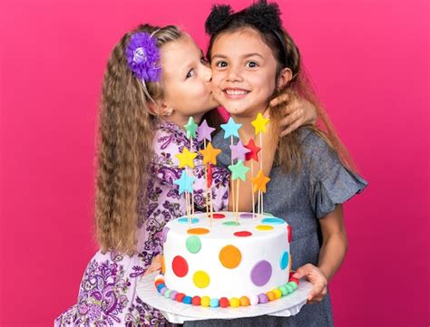 Heureuse petite fille blonde embrassant une petite fille caucasienne souriante tenant un gâteau