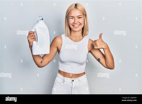Beautiful Blonde Woman Holding Detergent Bottle Smiling Happy And Positive Thumb Up Doing
