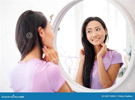 Smiling Beautiful Asian Woman Looking At Herself In The Mirror At Home