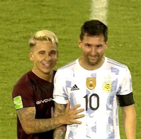 Two Men Standing Next To Each Other On A Soccer Field With Their Arms