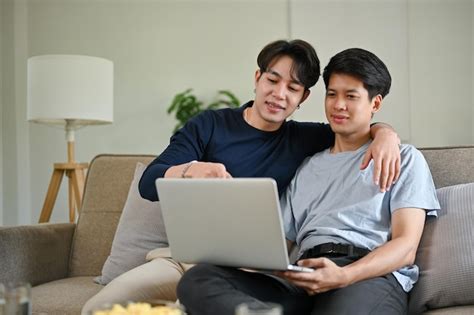 Un hombre gay asiático feliz disfruta viendo una película a través de una computadora portátil