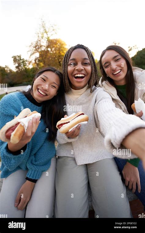 Vertical Group Cheerful Girls Selfie Eating Takeaway Street Food Sitting On Bench In Nice Area