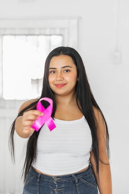 Mujer latina morena sosteniendo en su mano una cinta rosada símbolo de la lucha contra el cáncer