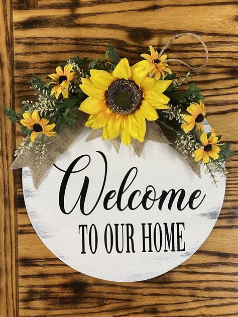 A Welcome Sign With Sunflowers And Greenery Hanging On A Wooden Door Frame